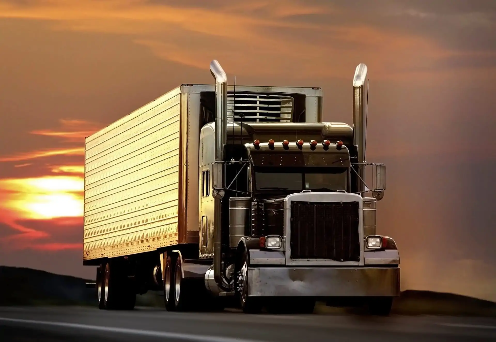 Semi-truck driving on the highway during sunset.