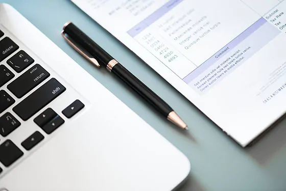 A pen sits next to a laptop on a table, hinting at possible law-related paperwork or writing.