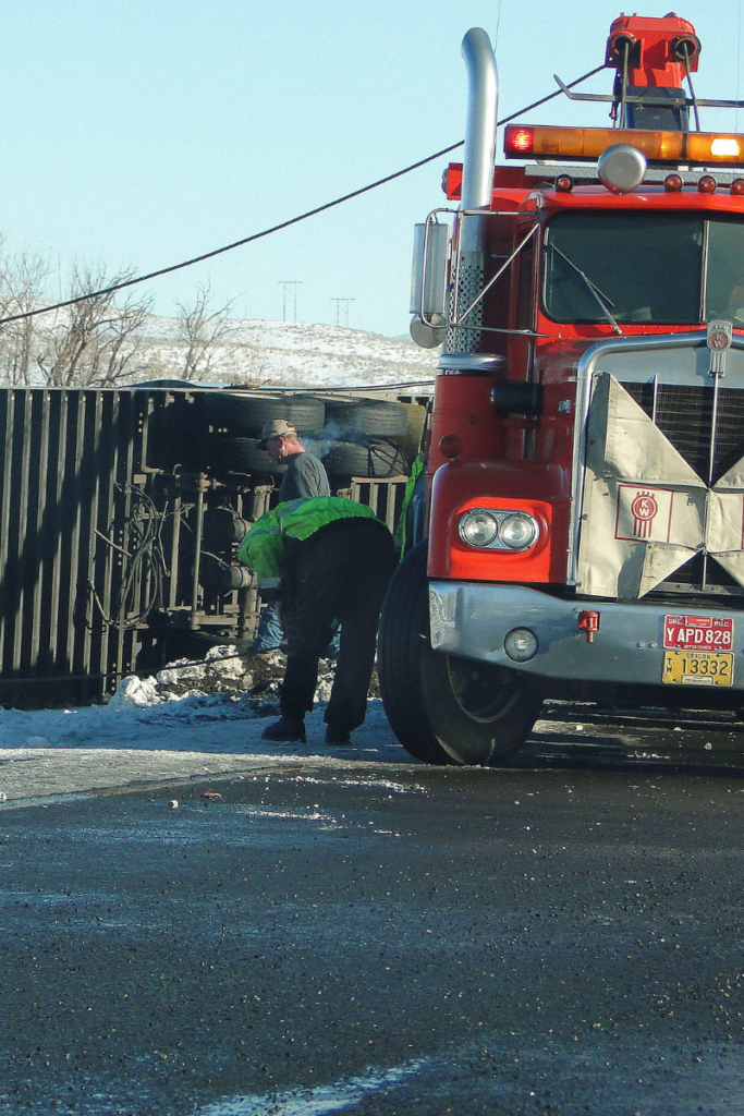 Man observing tire of semi-truck on side of the road.