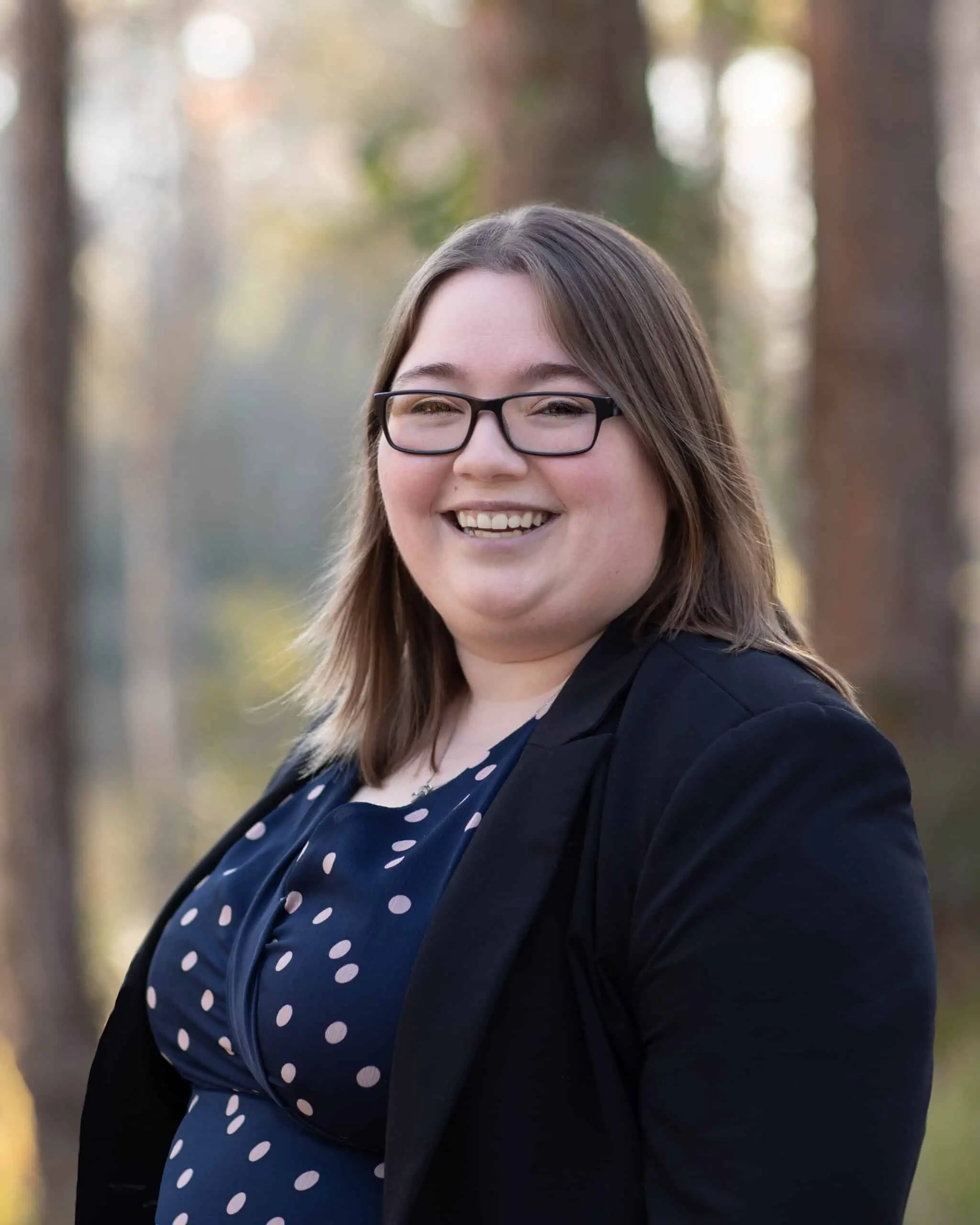 A smiling woman wearing glasses and a polka dot dress.