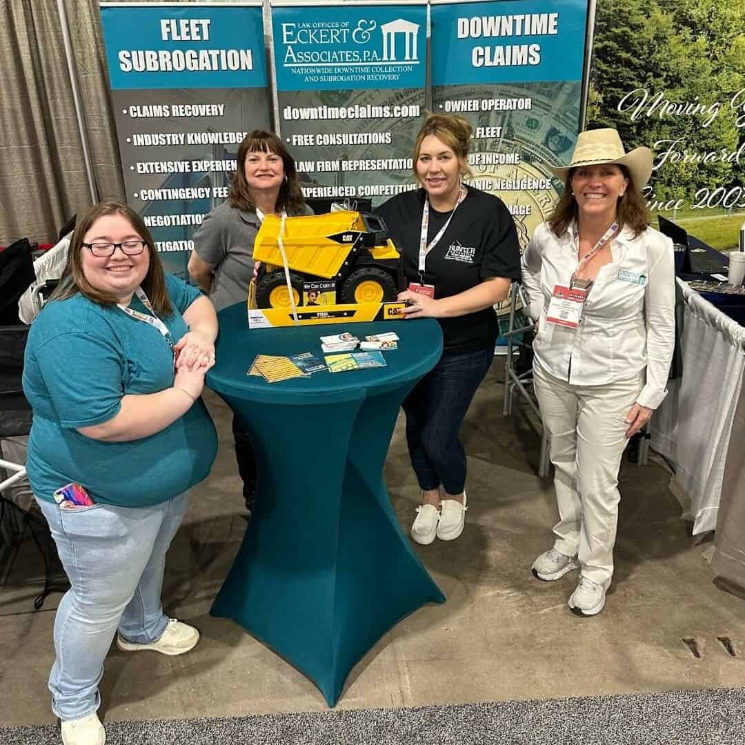 Four individuals at a trade show booth smiling for the camera.