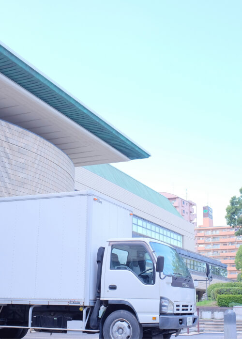 A white box truck is parked outside a modern building with curved, green-roofed architecture under a clear sky.