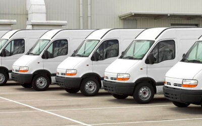A row of identical white vans parked in marked spaces outside an industrial building.